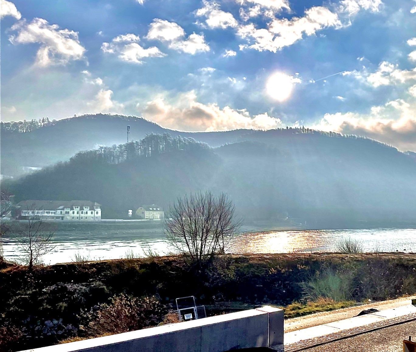 Slnečné lúče nad riekou s kopcami v pozadí.