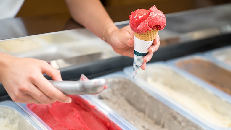 One hand holds an ice cream cone with a scoop of fruit ice cream, the other holds an ice cream scoop., © Blochberger Eisproduktion GmbH