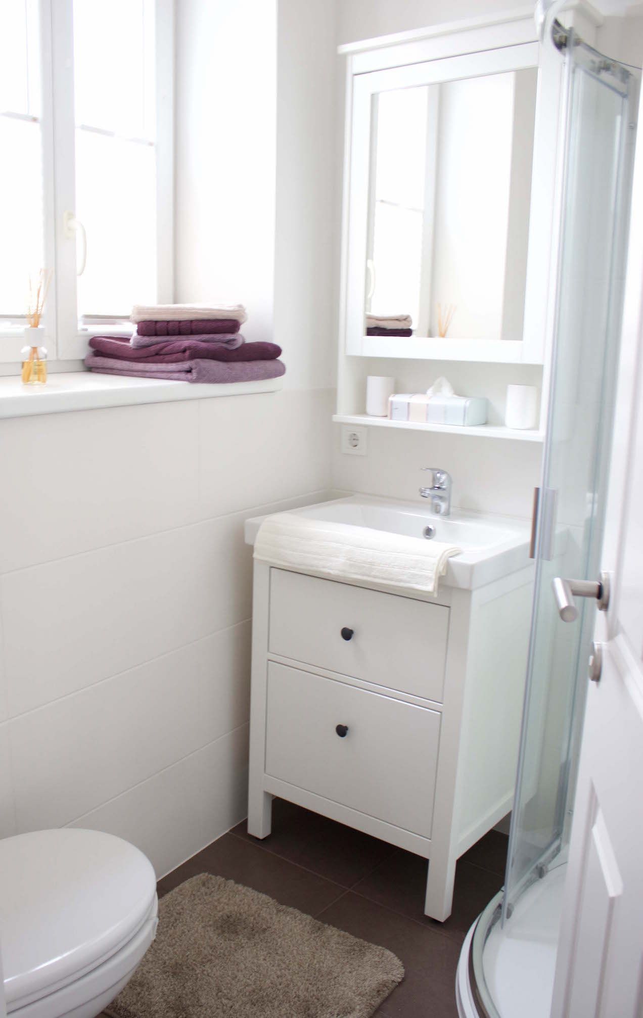 Moderná kúpeľňa s bielym umývadlom, zrkadlom, uterákmi a sprchovacím kútom.