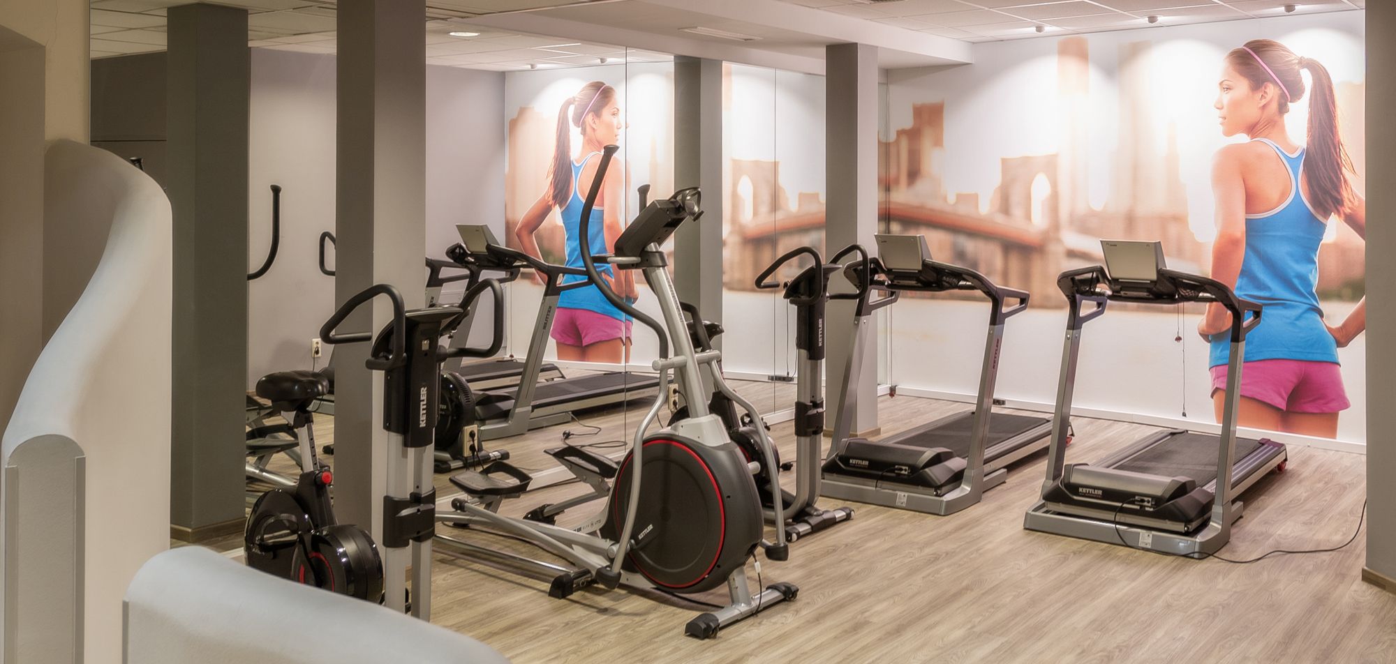 Posilňovňa s bežeckými pásmi a fitnes zariadeniami, nástenná maľba bežiacej ženy.