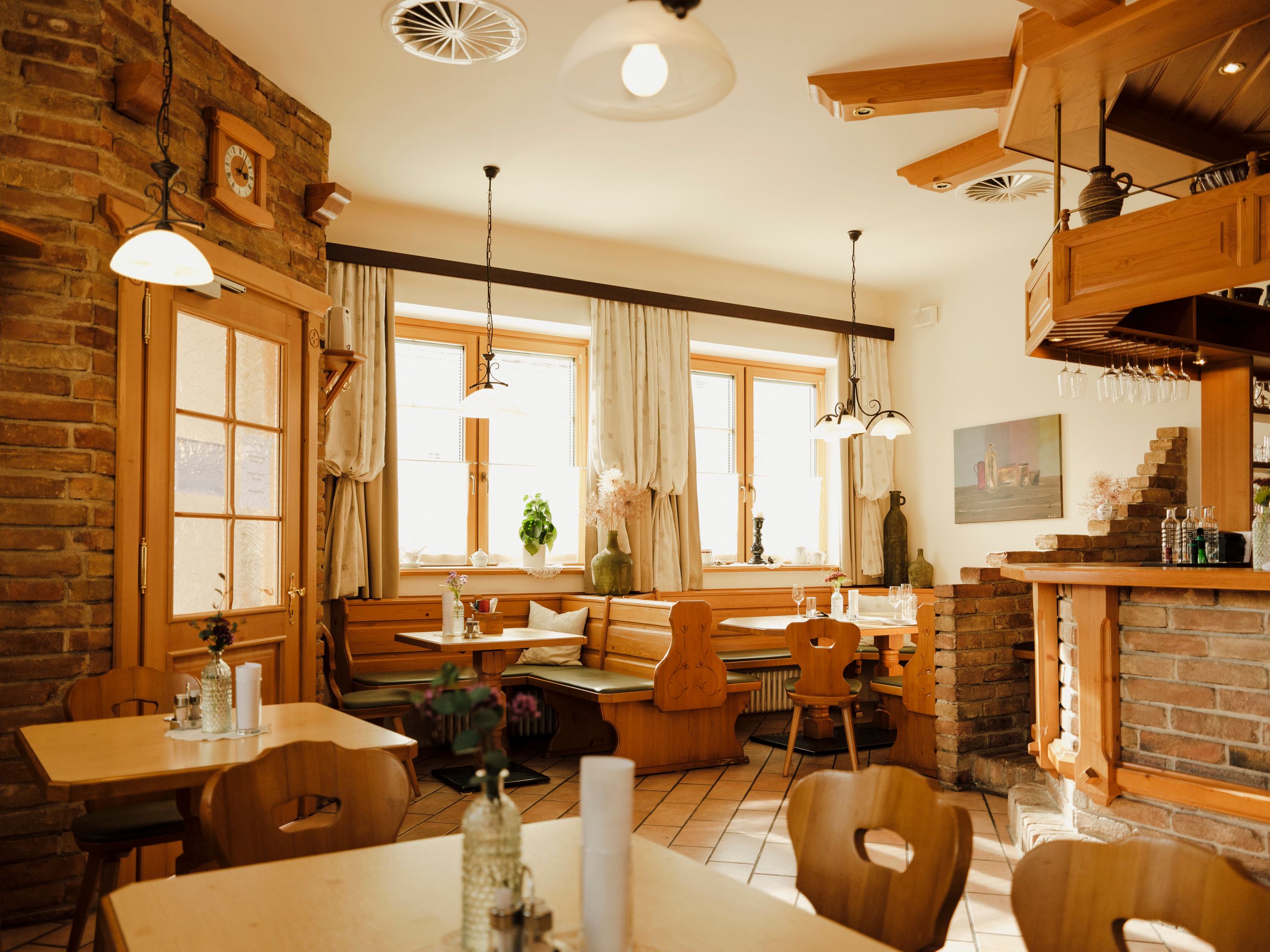 Útulná jedáleň s dreveným nábytkom a tehlovými stenami, zdobená rastlinami a lampami.