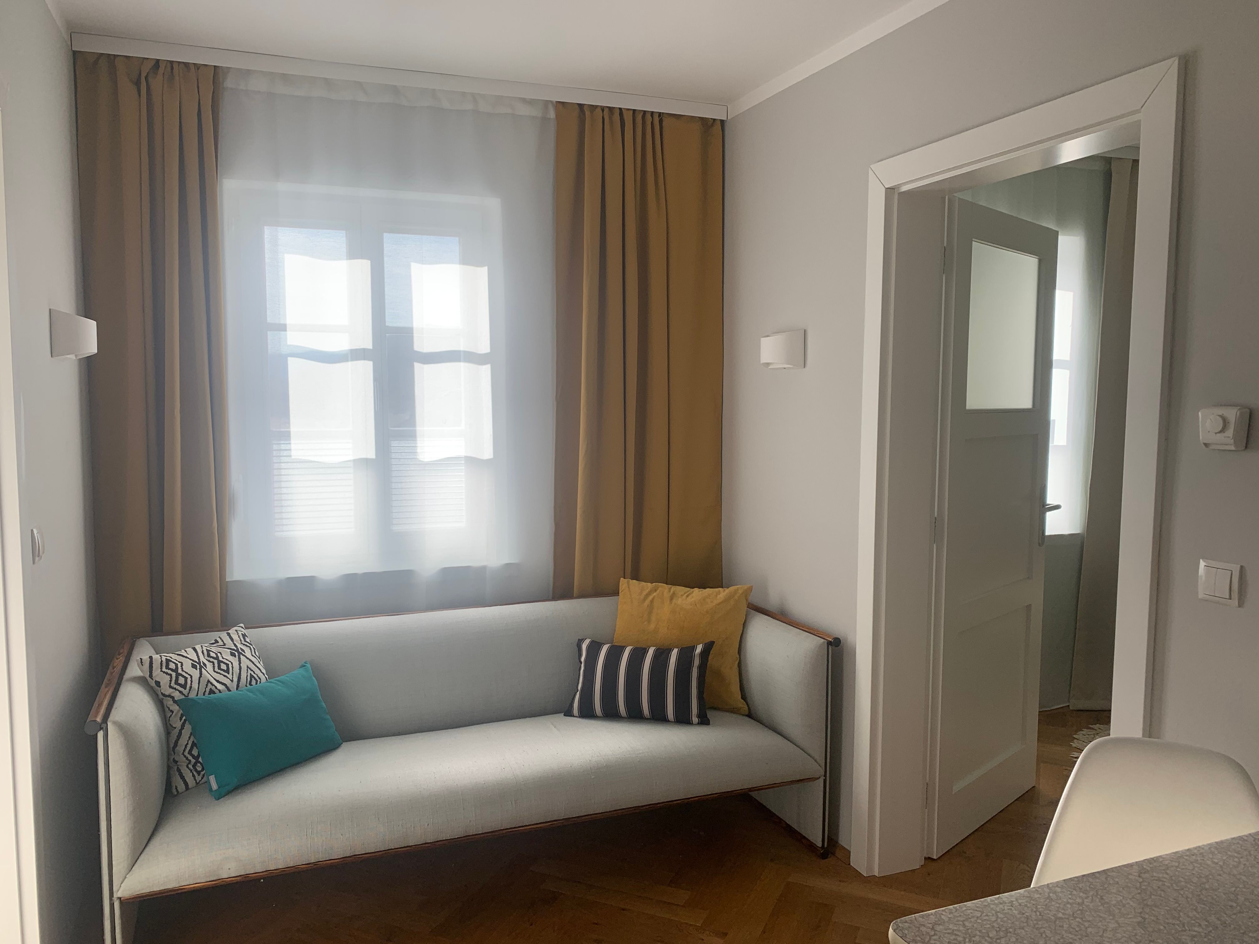 Útulná obývacia izba s pohovkou a vankúšmi, žltými závesmi a otvorenou zárubňou.