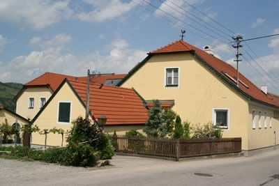 Žltý dom s červenou strechou vo vidieckom prostredí.