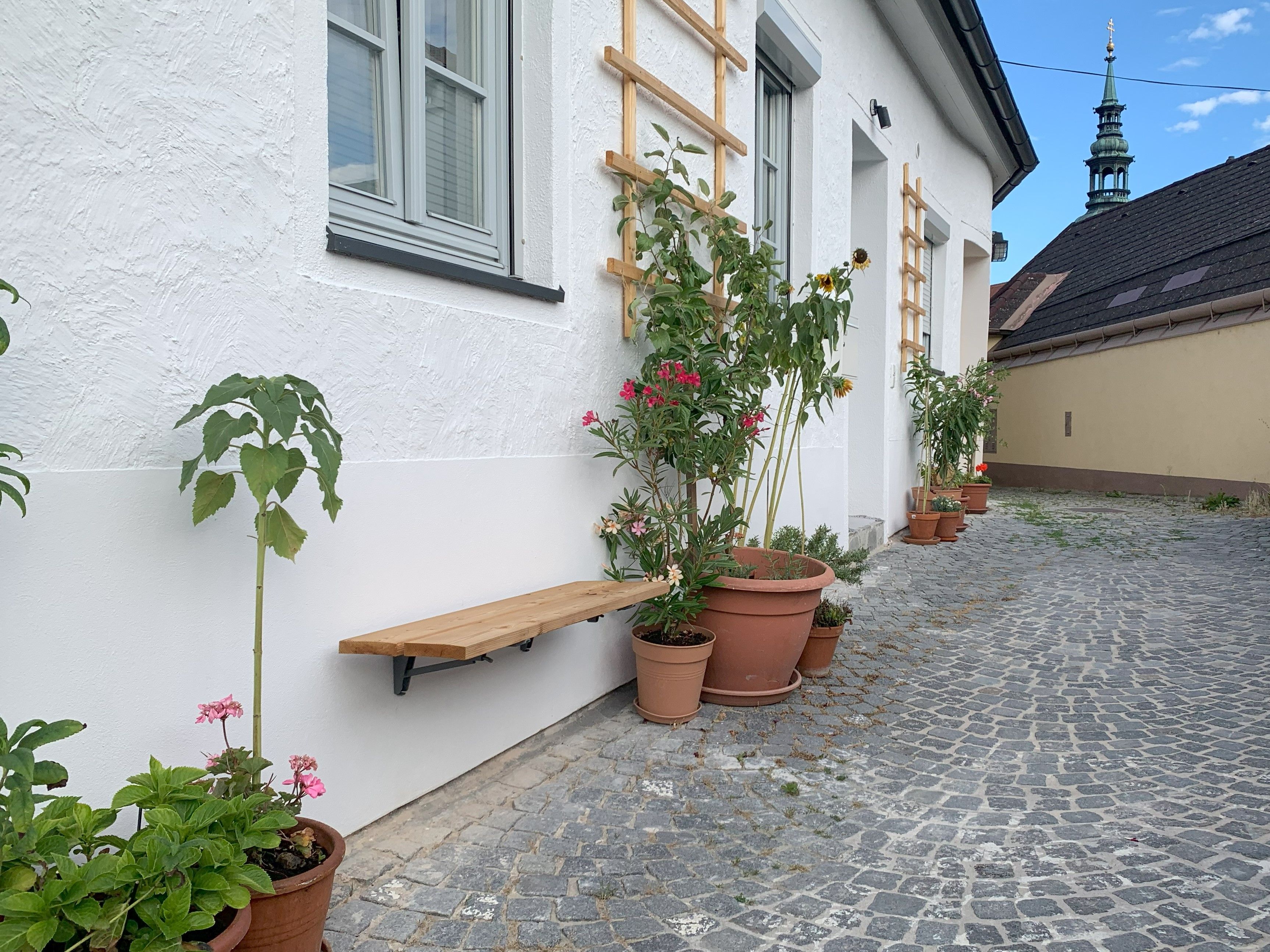 Vydláždená cesta s rastlinami v kvetináčoch pred bielou budovou.