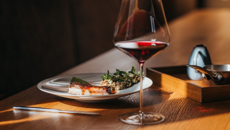 Na drevenom stole tanier s jahňacím bôčikom, šalátom a wasabi krémom a pohár červeného vína.