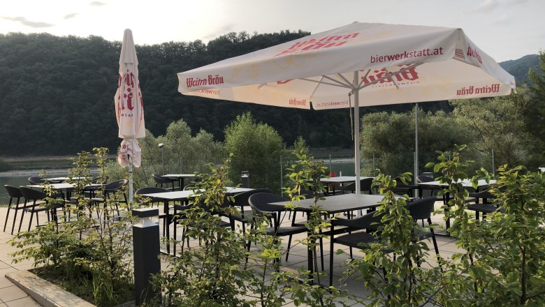 Terasa so stolmi, stoličkami a slnečn&iacute;kmi, obklopen&aacute; pr&iacute;rodou.