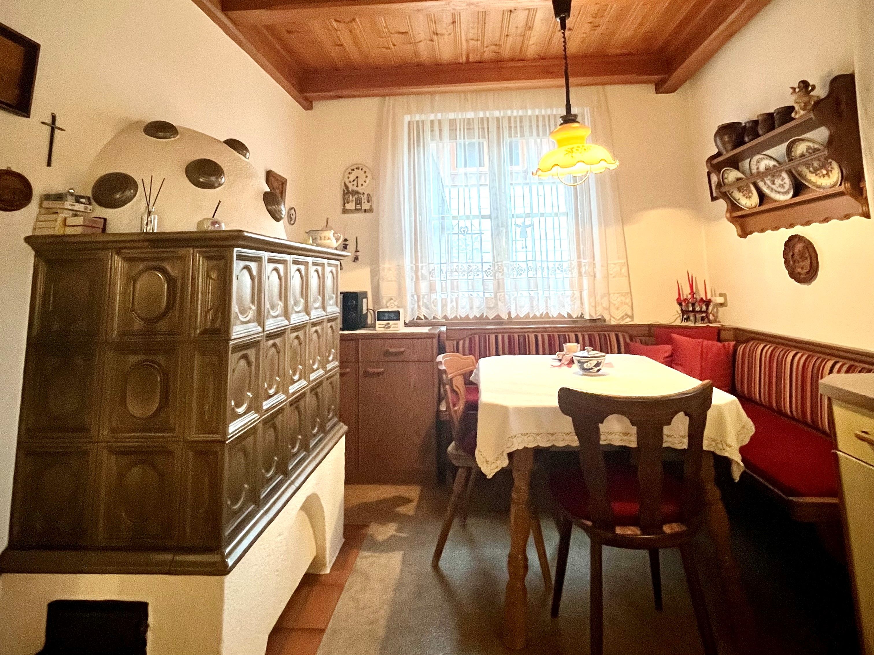 Útulná kuchyňa s kachľovou pecou, dreveným stolom a rohovou lavicou.