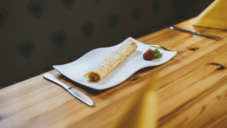 Palacinka na bielom tanieri s jahodami a mätou, podávaná na drevenom stole.
