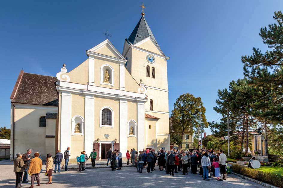 Ľudia sa za slnečného počasia zhromažďujú pred kostolom s vežou a hodinami.
