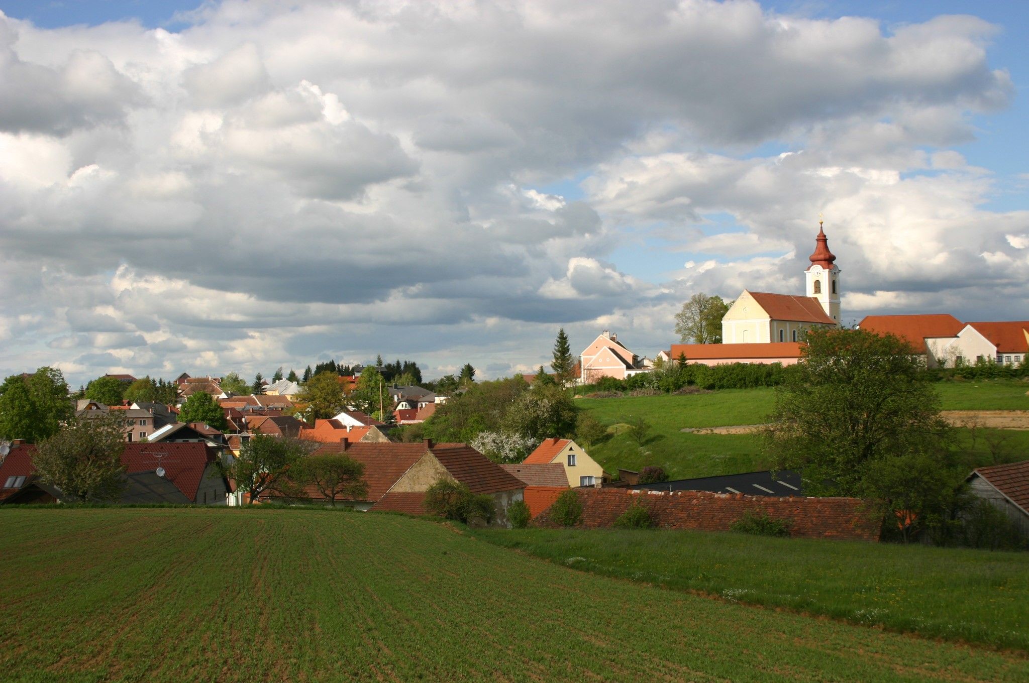 Krajina s dedinou a kostolom pod zamračenou oblohou.