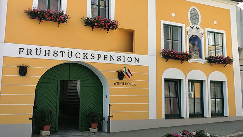 Žltý domček pre hostí so zelenými dverami a kvetinovými truhlíky.