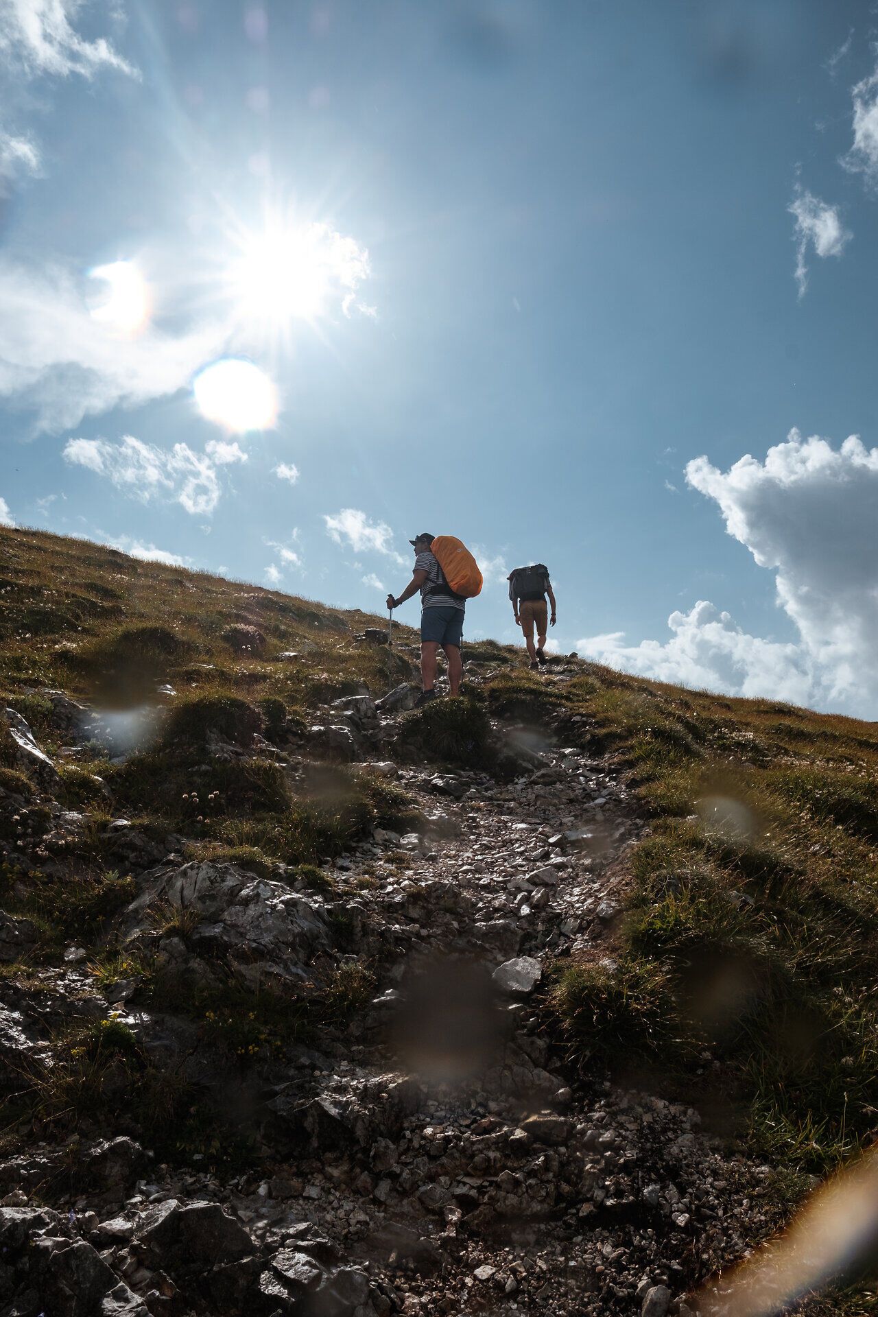 Turisti stúpajú po miernom svahu, obklopení sviežou zeleňou a žiarivým svetlom slnka. Svieži horský vzduch a úchvatné výhľady vás pozývajú vychutnať si krásu prírody naplno.