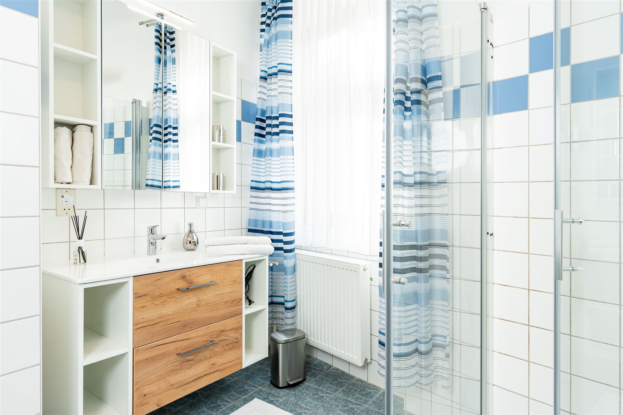 Moderná kúpeľňa s drevenou skrinkou, zrkadlom, sprchovým závesom a obkladmi.