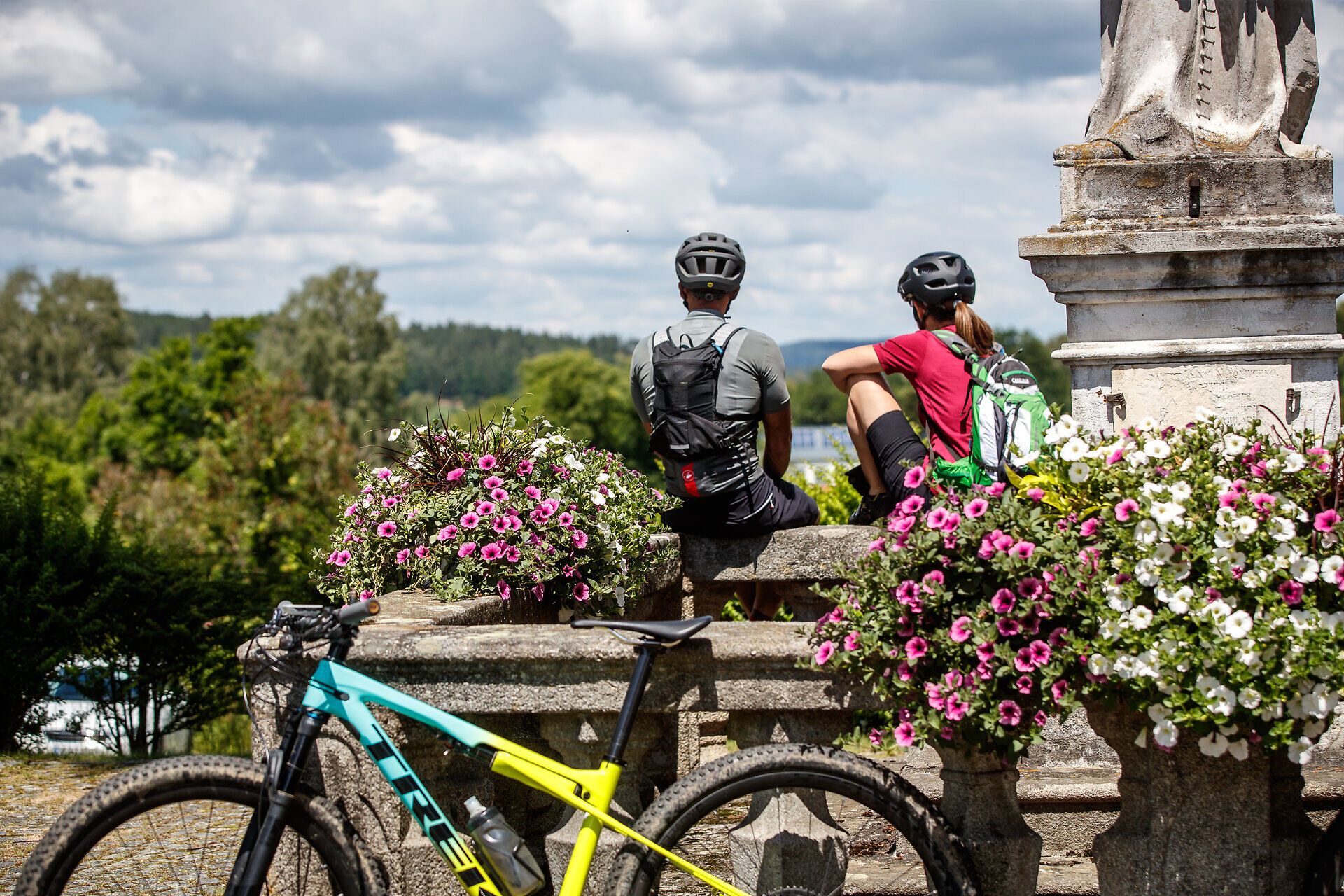 Dvaja horskí cyklisti si užívajú zaslúžený oddych uprostred rozkvitnutej krajiny. Toto miesto obklopené pestrofarebnými kvetmi a sviežim horským vzduchom ponúka dokonalú kulisu pre dobrodružstvá v prírode.