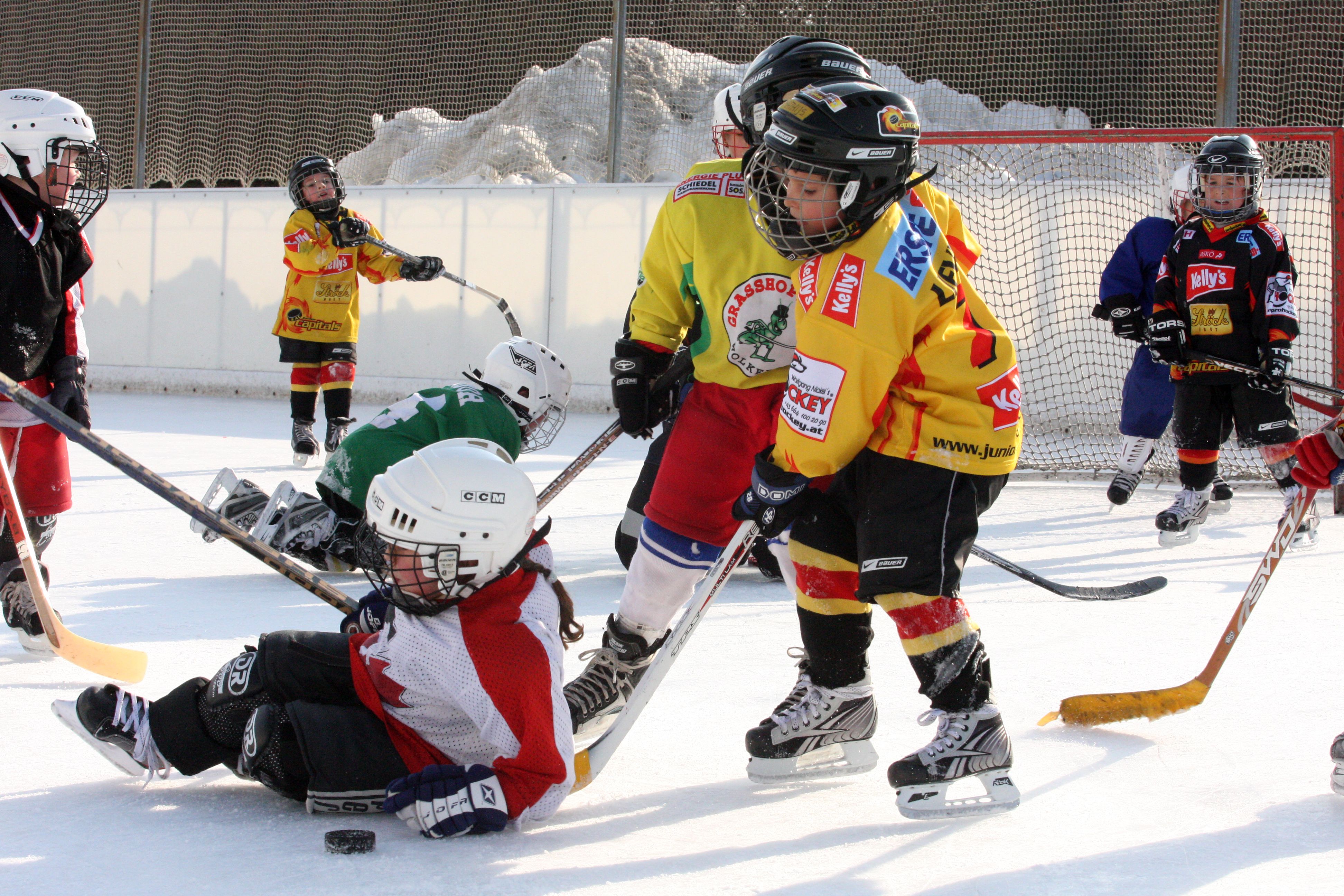 Deti hrajú hokej na vonkajšom klzisku.