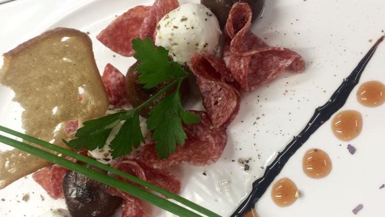 Tanier so salámou, guľôčkou kozieho syra, bylinkami a kúskom chleba.