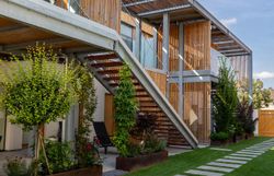 Moderná budova s bielou fasádou a drevenými prvkami, obklopená múrom s drevenou bránou.