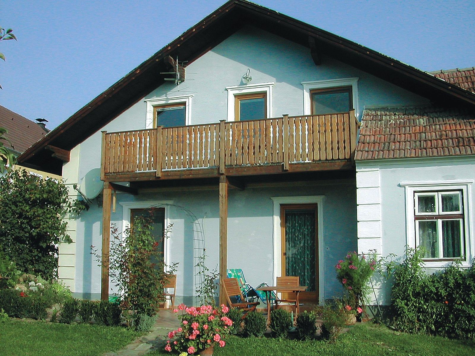 Tradičný vinohradnícky dom s dreveným balkónom a záhradným nábytkom pred dverami.