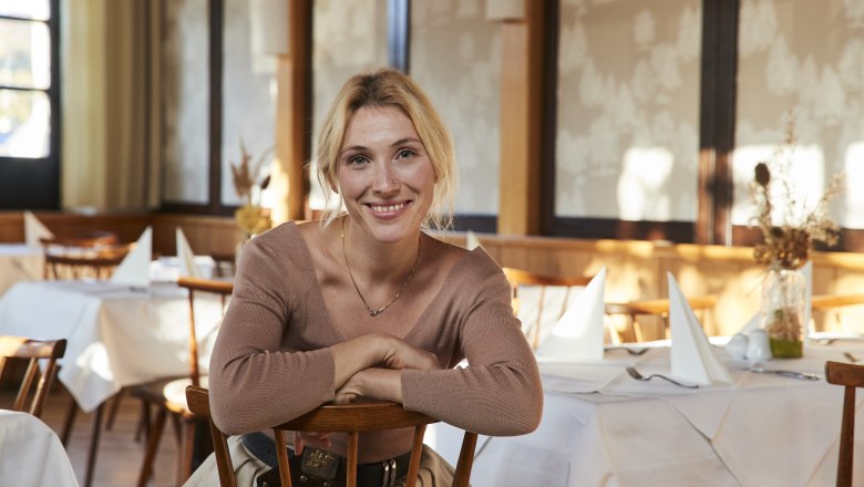 Žena sediaca s úsmevom v reštaurácii s prestretými stolmi.