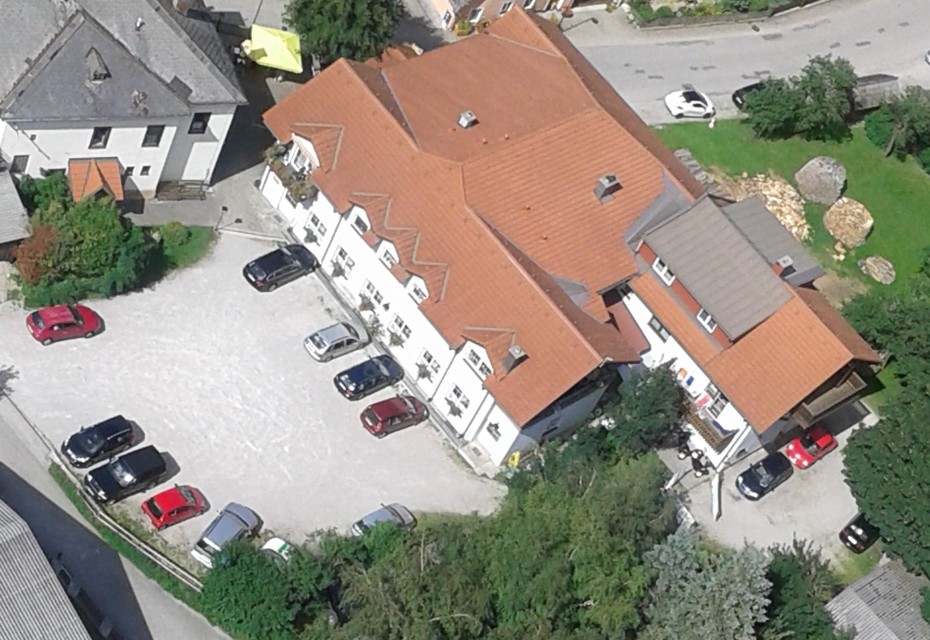 Letecký pohľad na komplex budov s červenými strechami a niekoľko zaparkovaných áut na parkovisku.