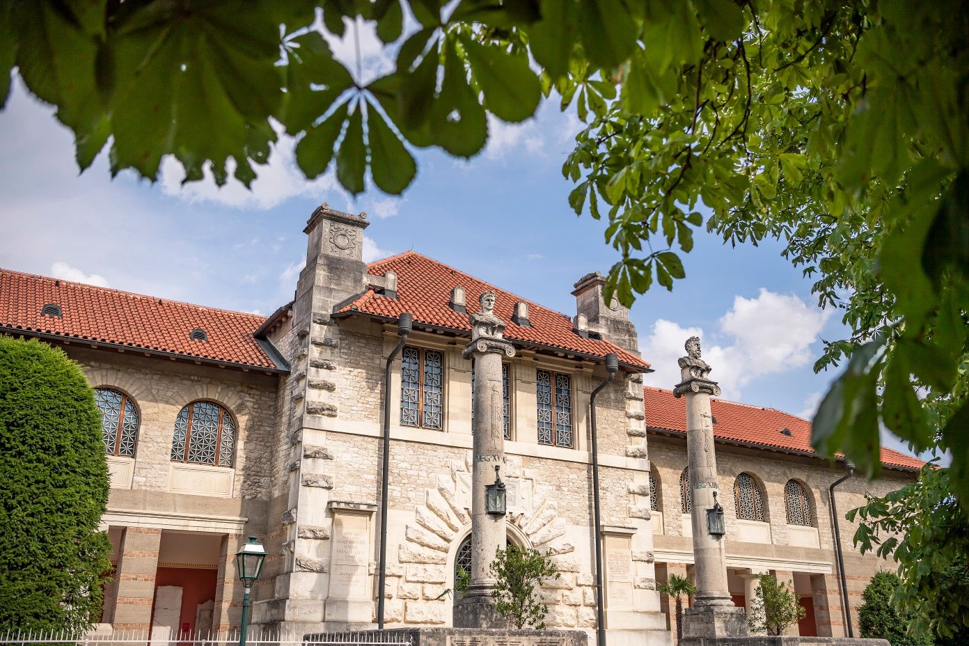 Exteriérový pohľad na múzeum Carnuntinum v Bad Deutsch-Altenburgu so stĺpmi a červenou škridlovou strechou, obklopené zelenými stromami.