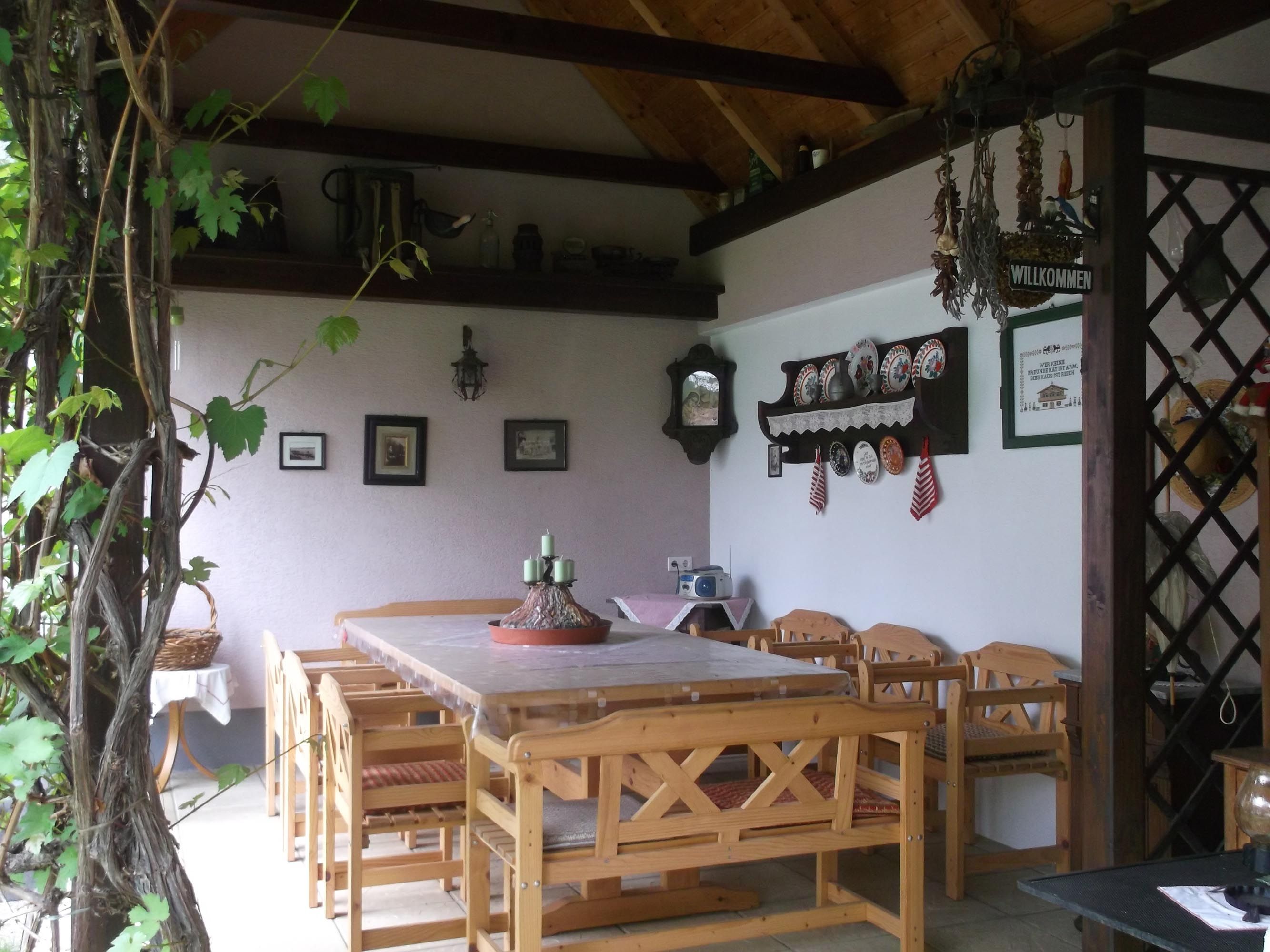 Krytá terasa so stolom a stoličkami, v pozadí stena s rôznymi nástennými dekoráciami.