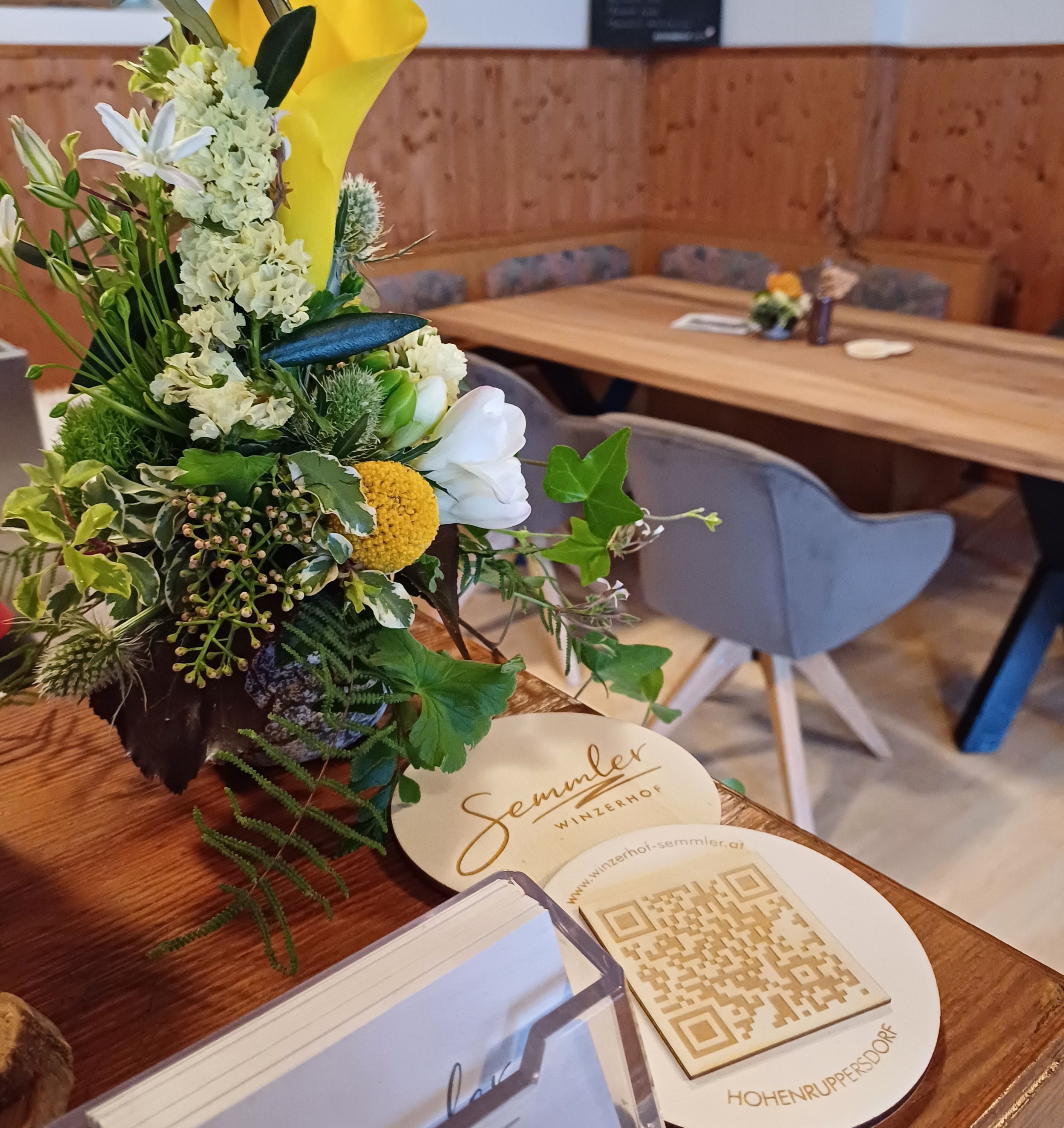 Kvetinová výzdoba na stole v hoteli Winzerhof Semmler s QR kódom a vizitkami.