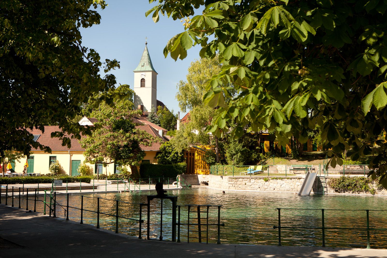 Termálne kúpele Bad Fischau-Brunn s kostolom v pozadí, obklopené stromami.