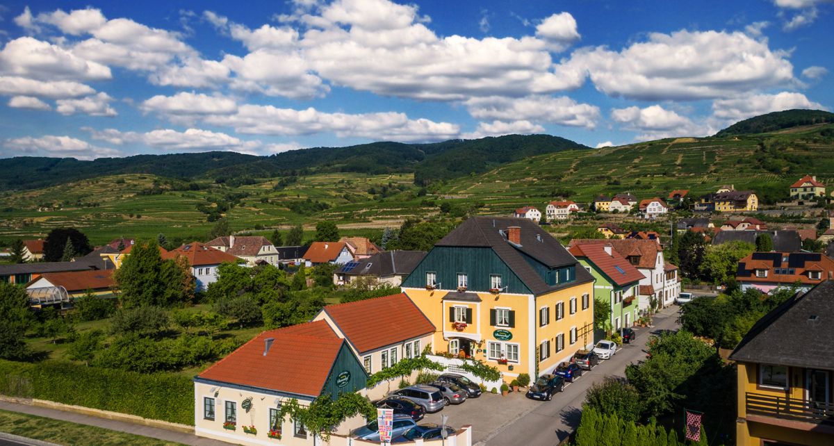 Vidiecke domy v zelenej kopcovitej krajine pod modrou oblohou s mrakmi.