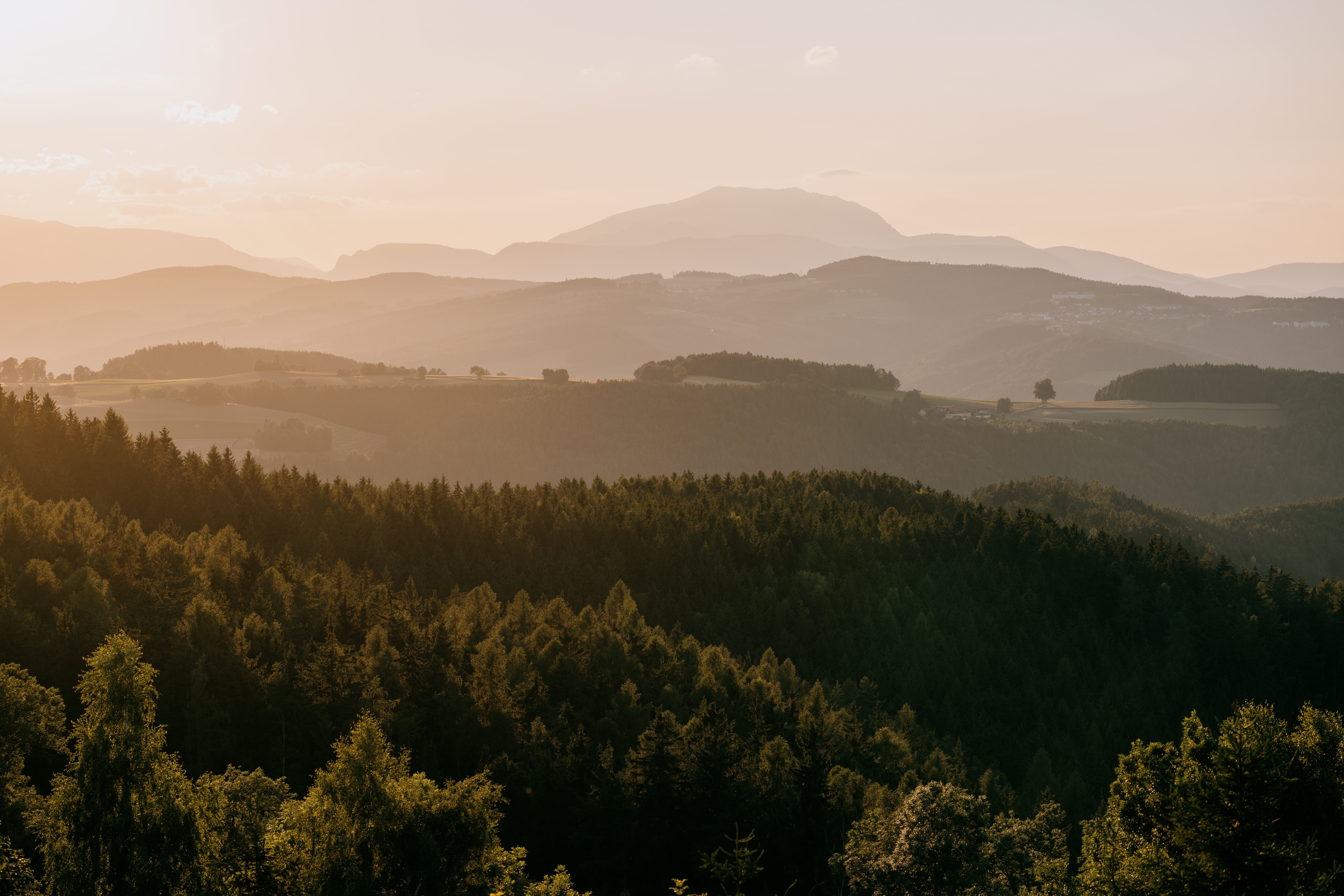 Západ slnka nad zalesnenou kopcovitou krajinou so zasneženou horou v pozadí.
