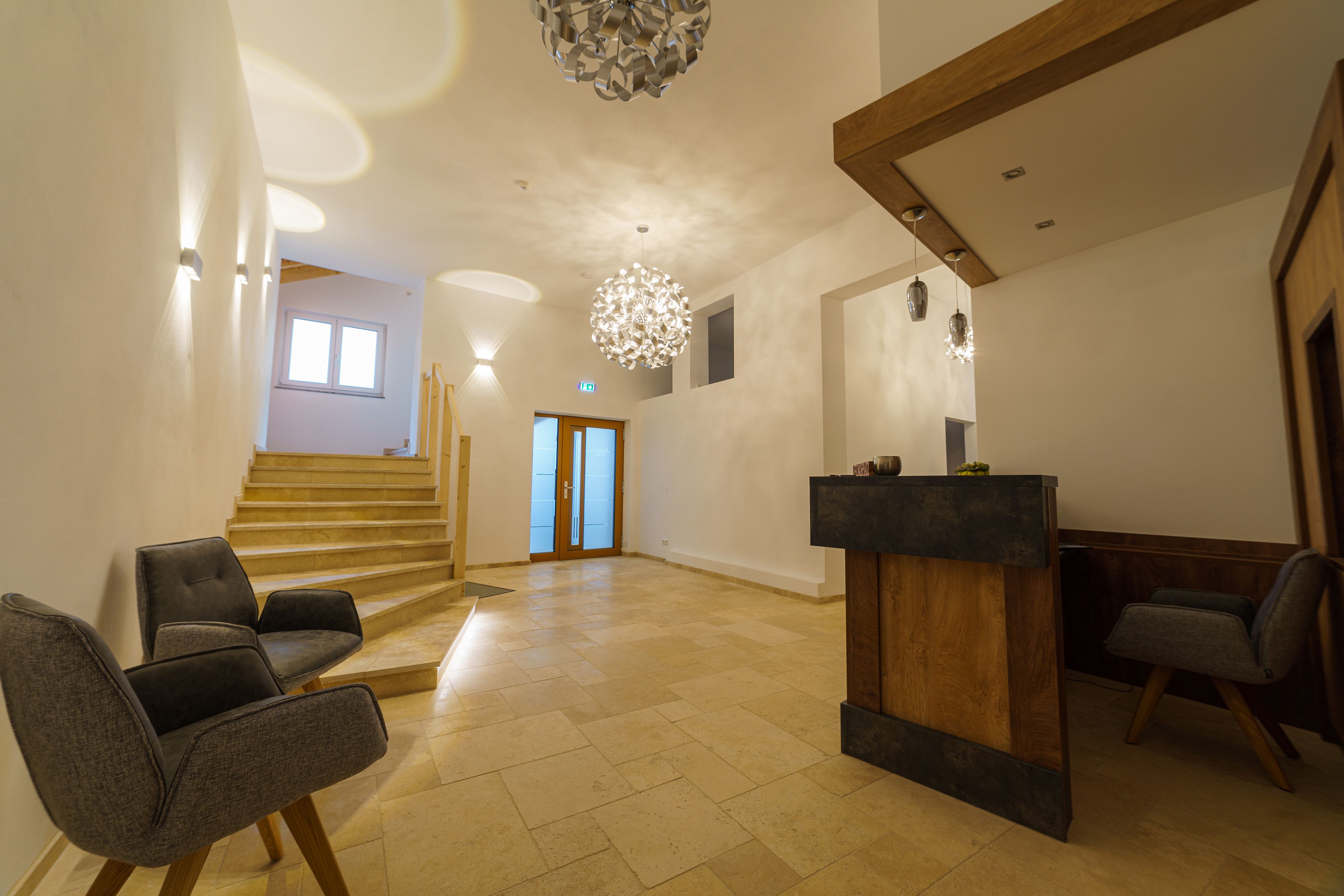 Moderná recepcia s dreveným pultom, dvoma sivými kreslami a schodmi.