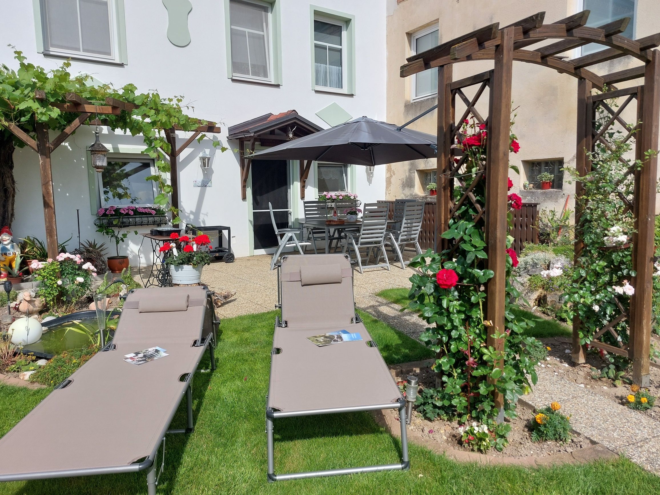 Záhrada s ležadlami, pergolou a kvetinami.