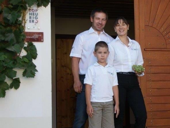 Rodina stojí pred budovou s drevenými dverami, žena drží hrozno.