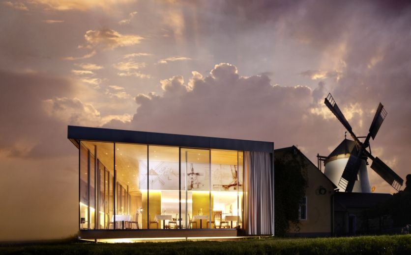 Moderná sklenená architektúra vedľa tradičného veterného mlyna pri západe slnka.