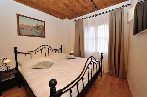 Spálňa s kovovou posteľou, drevenou podlahou a maľbou na stene.