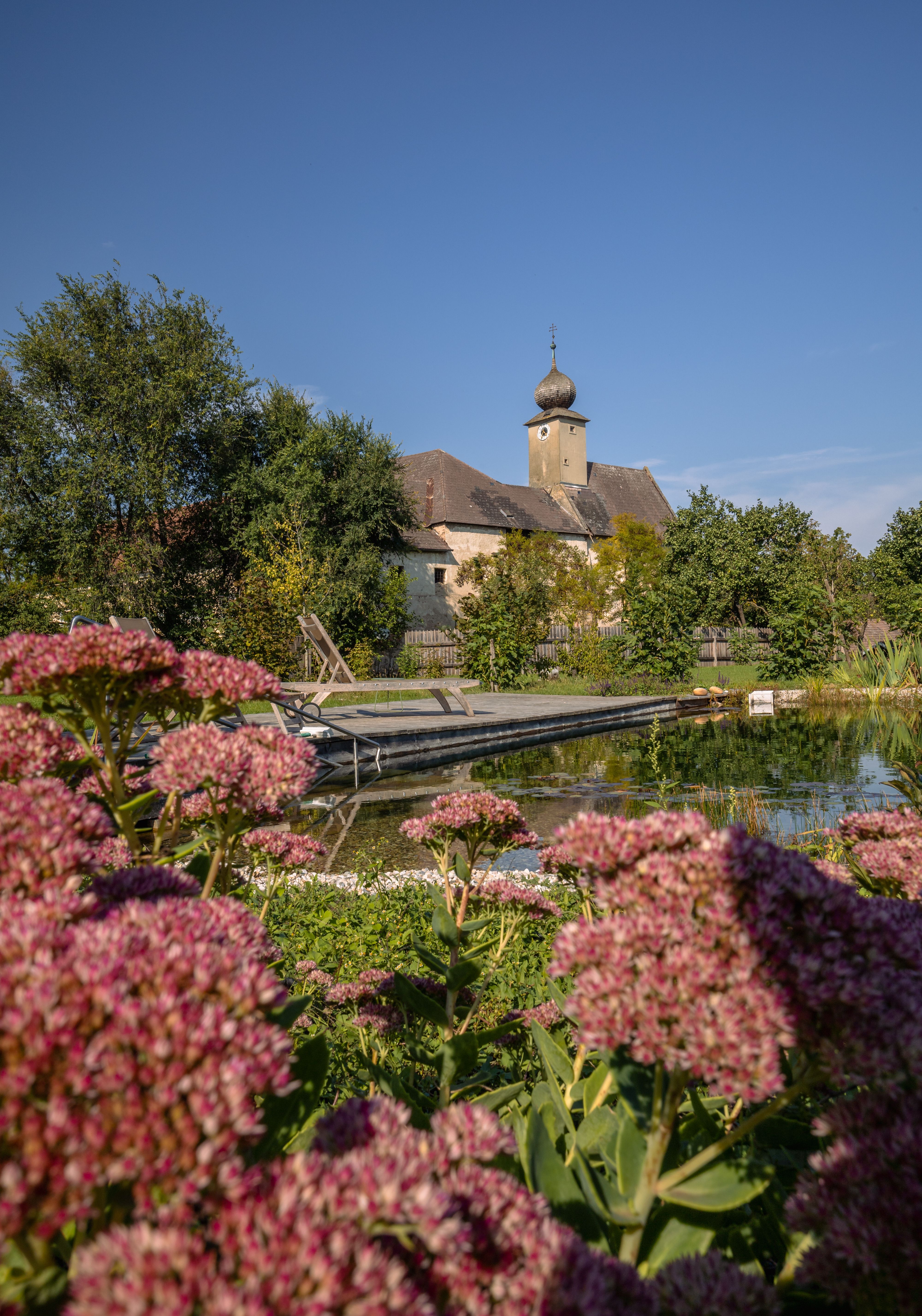 Spálňa s klenutým stropom, drevenou podlahou, posteľou, kreslom, komodou a kožušinovým kobercom.