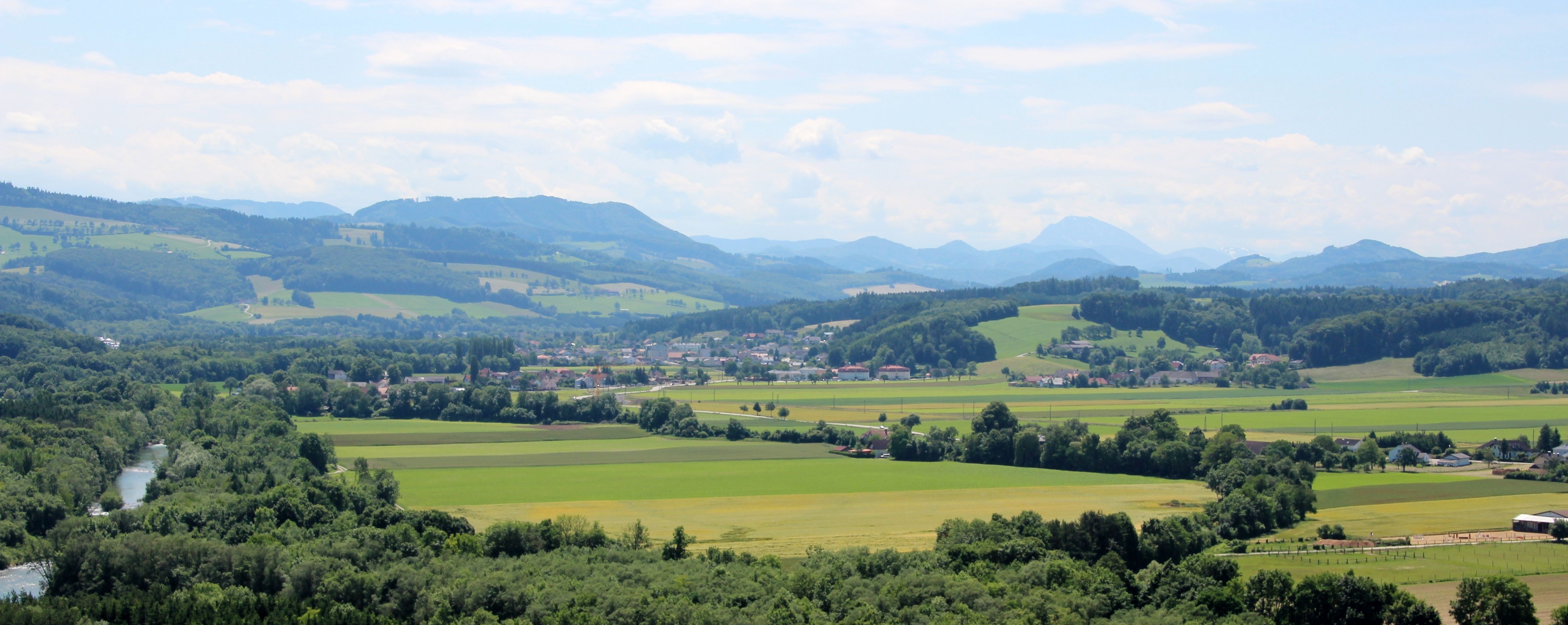 Panoráma zelenej krajiny s kopcami, poliami a riekou.