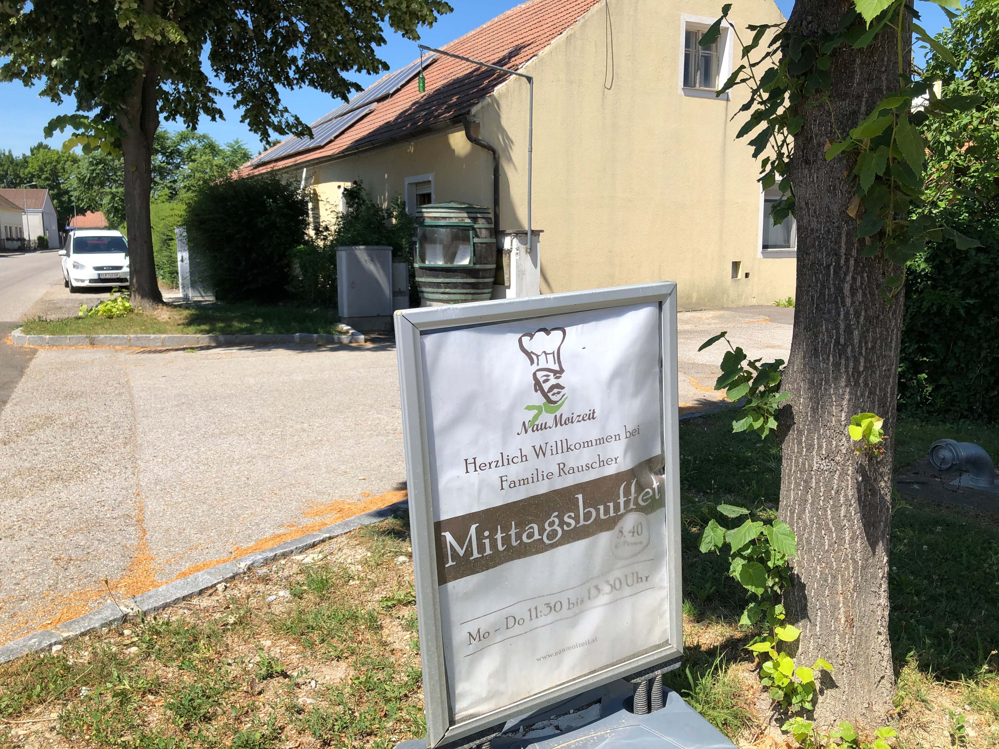 Nápis pred budovou s nápismi "Mittagsbuffet" a "Herzlich Willkommen bei Familie Rauscher".