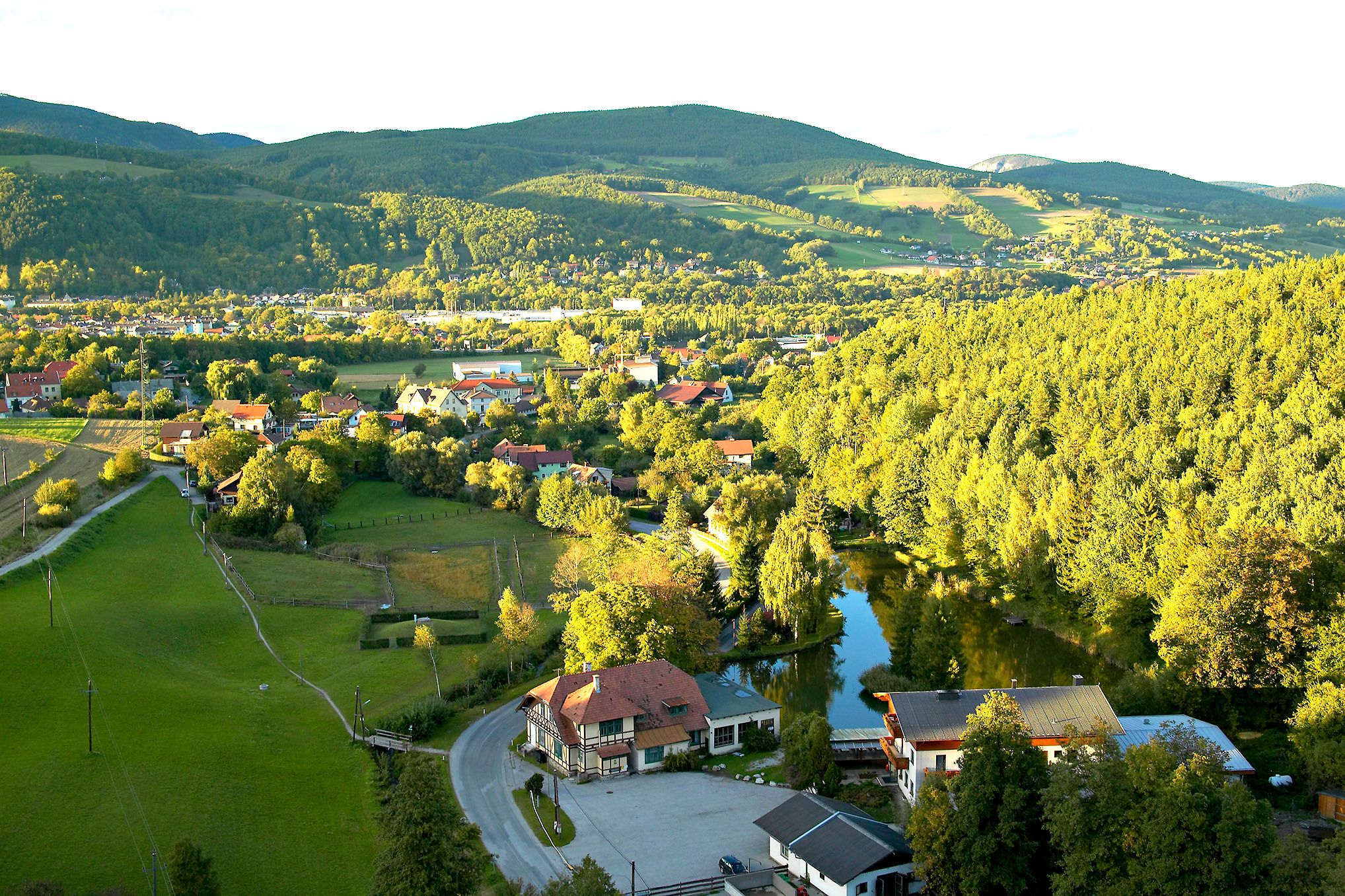 Pohľad na krajinu Enzenreith s domami, lesmi a kopcami v pozadí.