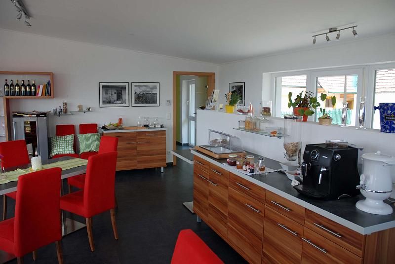 Raňajková miestnosť s červenými stoličkami, dreveným nábytkom a kávovarom.