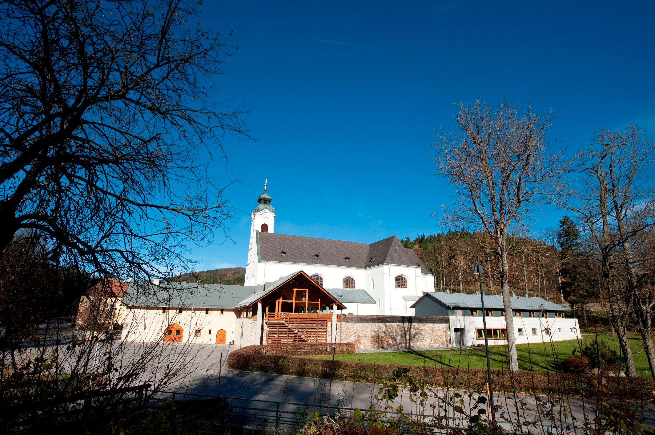 Pútnický kostol Klein-Mariazell s modrou oblohou a stromami v popredí.