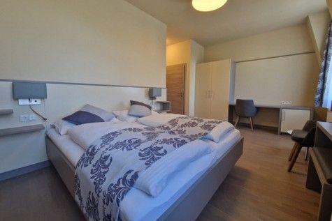 Moderne zariadená hotelová izba s manželskou posteľou, písacím stolom a šatníkovou skriňou.