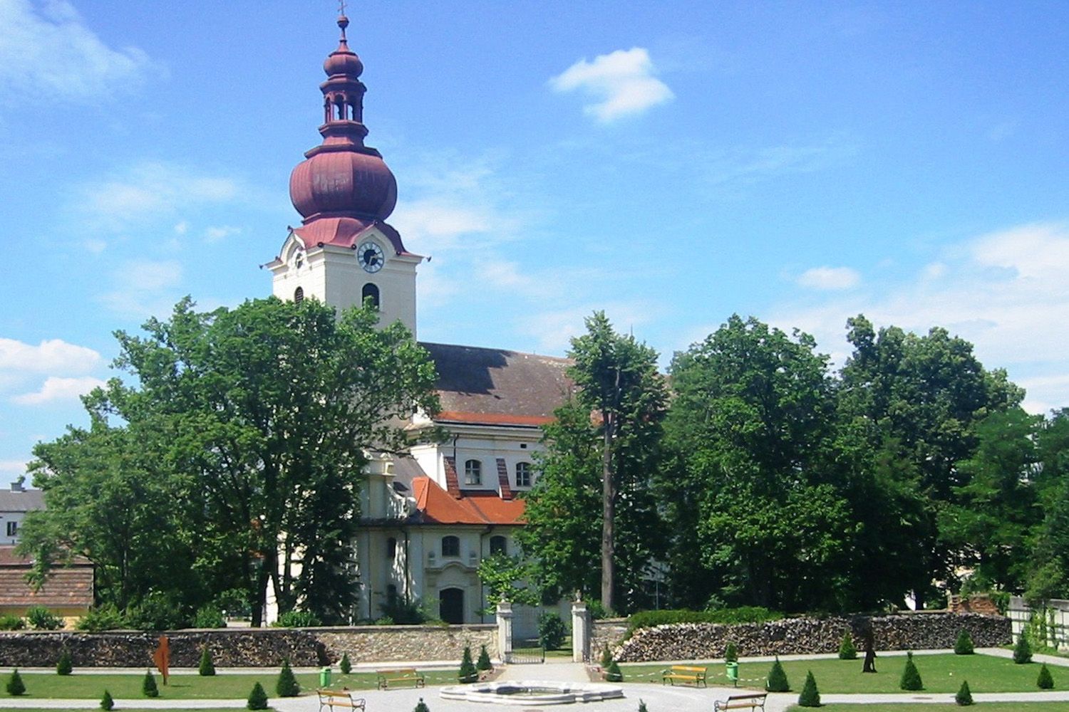 Barokový kostol s červenou vežou a barokovou záhradou v popredí.