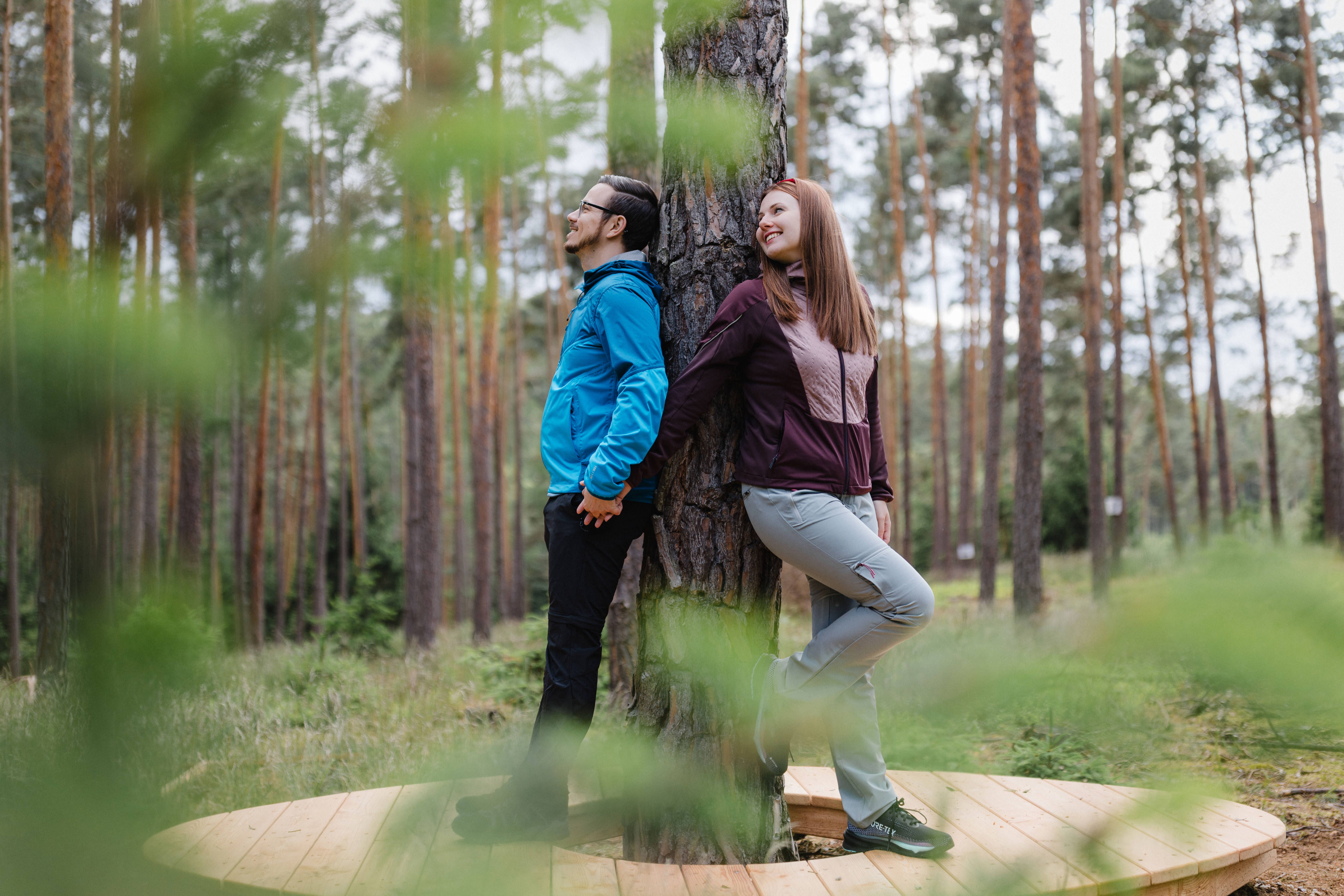 Dvaja ľudia opretí o strom v lese stoja na drevenej plošine.