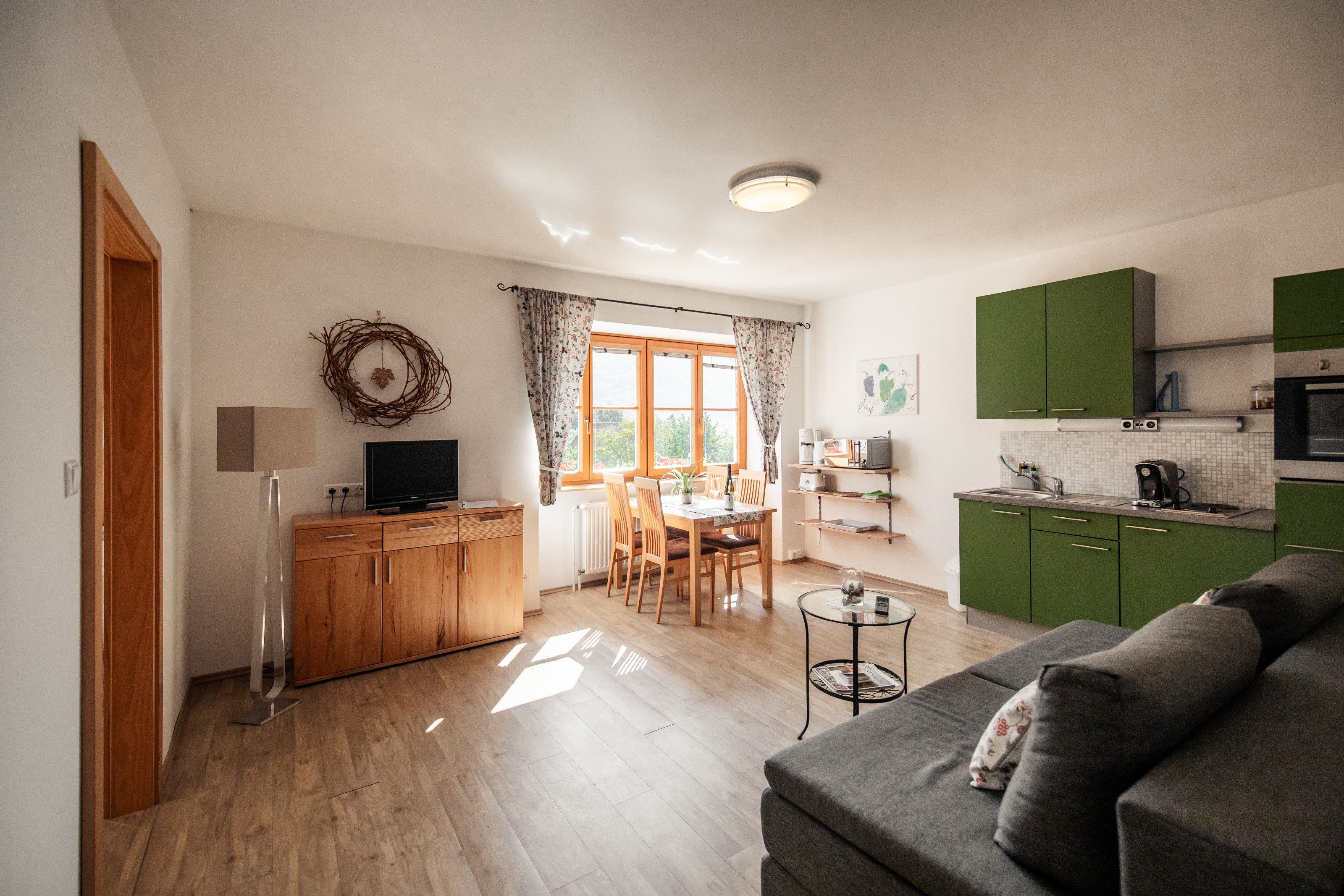 Svetlá obývacia izba so zelenou kuchyňou, jedálenským stolom a pohovkou.