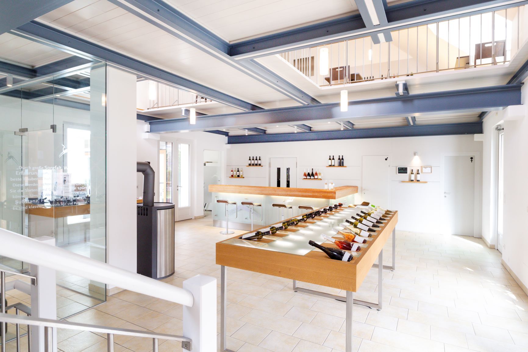 Pohľad do interiéru modernej vinárne s fľašami vína na stole a barom v pozadí.