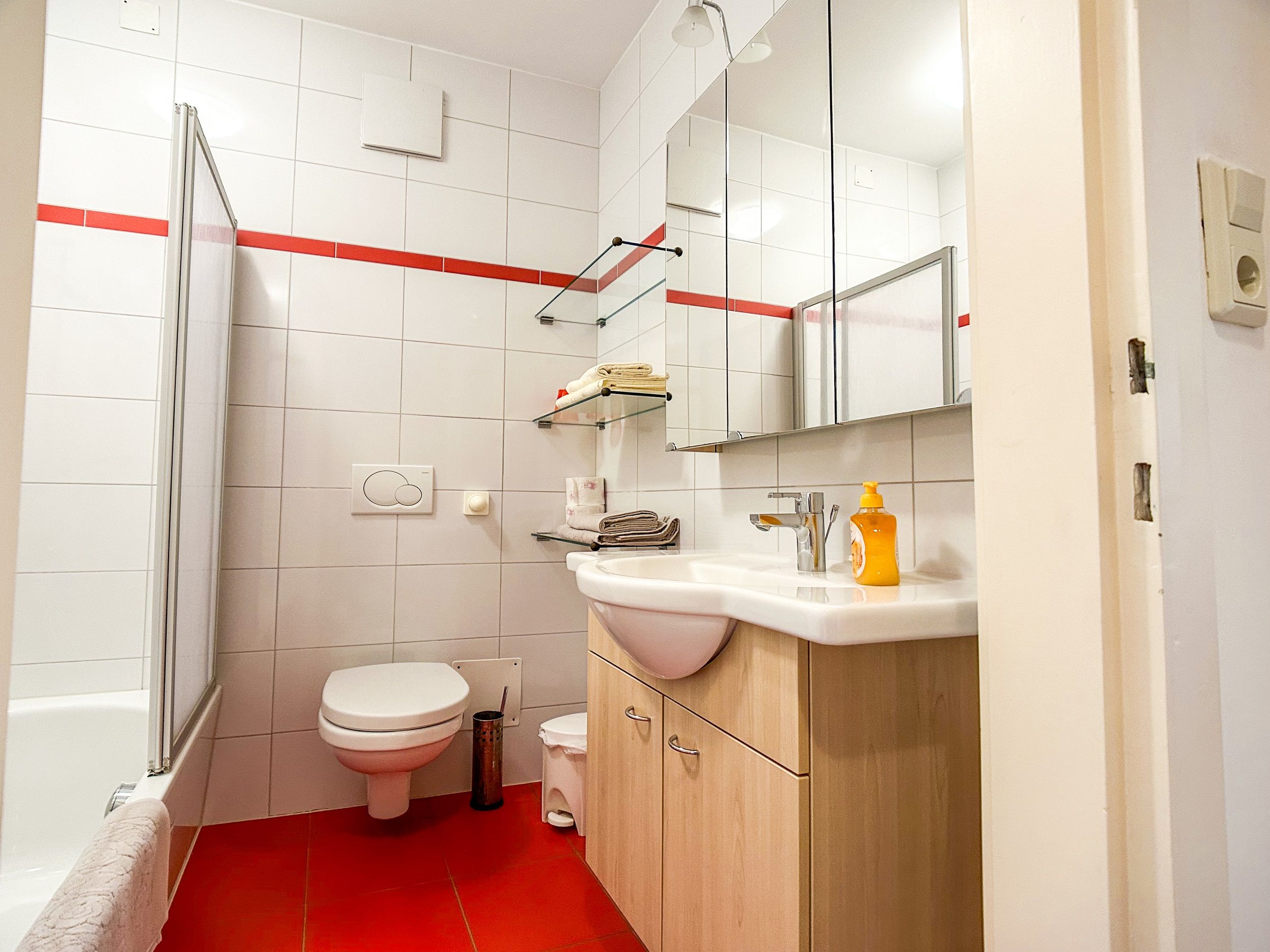 Moderná kúpeľňa s červenými obkladačkami, bielou keramikou a zrkadlami.