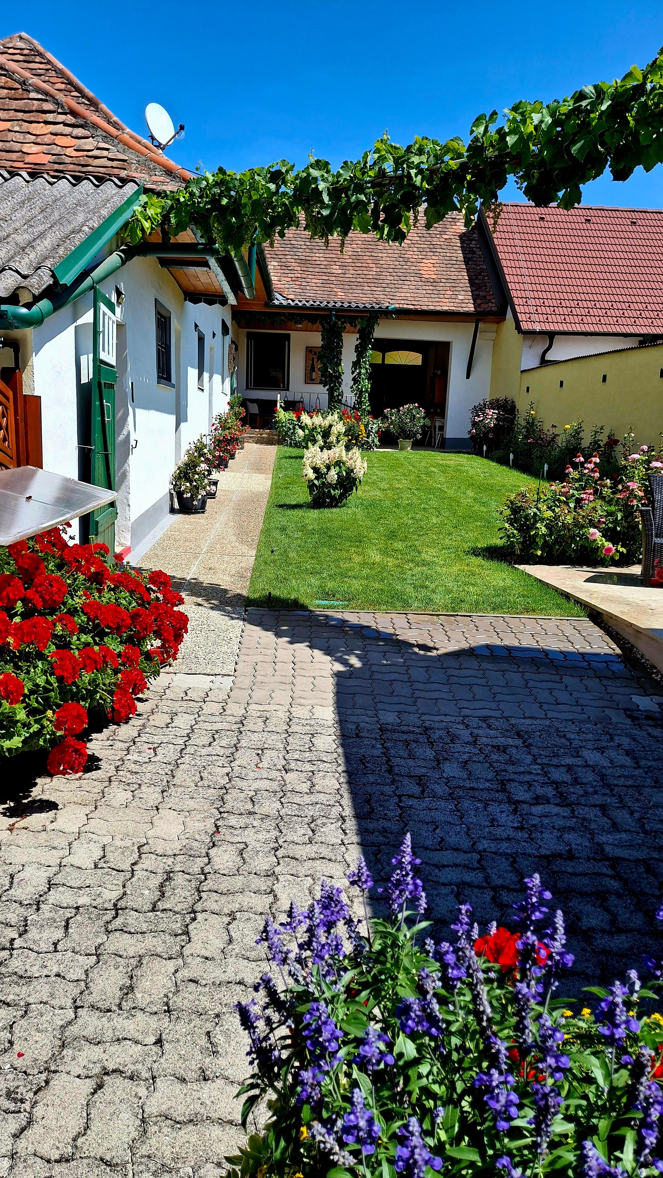Malebné vnútorné nádvorie rekreačného domu s kvitnúcimi kvetmi a upraveným trávnikom pod jasne modrou oblohou.