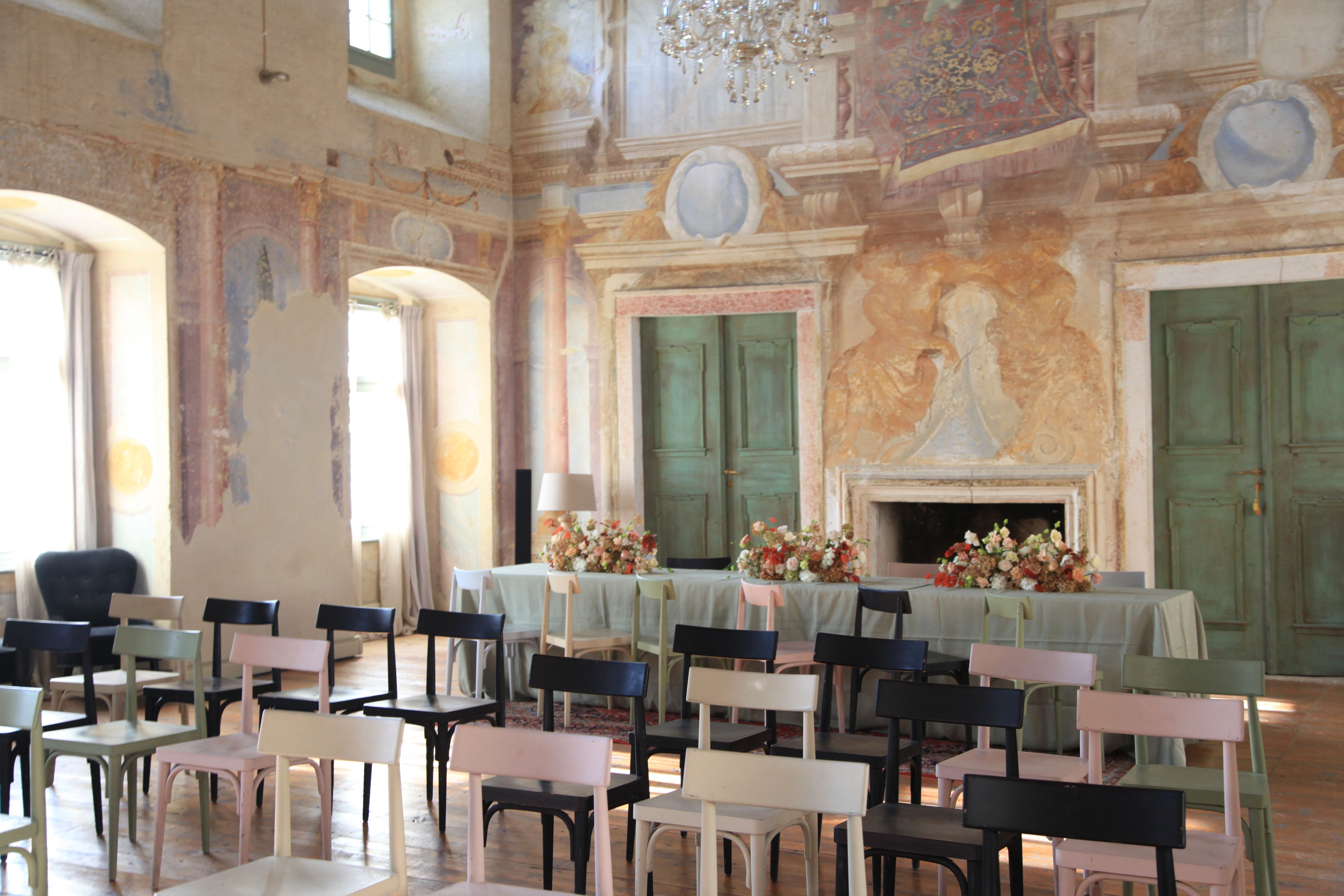 Sviatočne vyzdobená sála s pomaľovanými stenami, stoličkami a stolom s kvetmi.