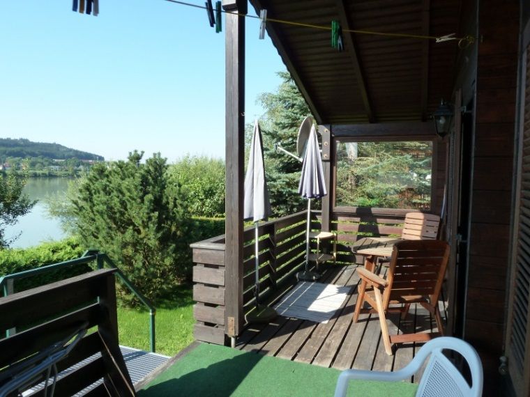 Drevená terasa rekreačného domu s výhľadom na jazero a zelenú krajinu.